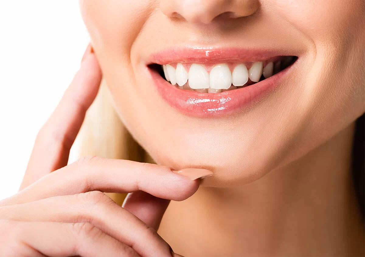 Smiling person with white teeth and glossy pink lips, a hand touching their chin.