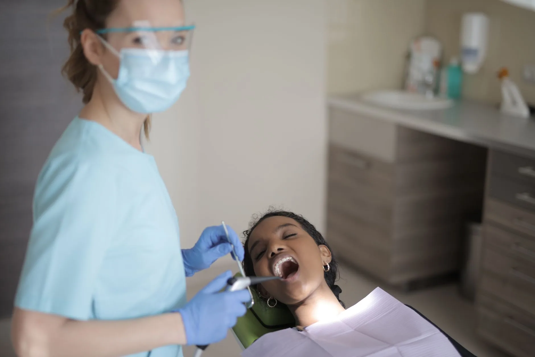 A dental professional performs a routine exam for a patient in a treatment chair